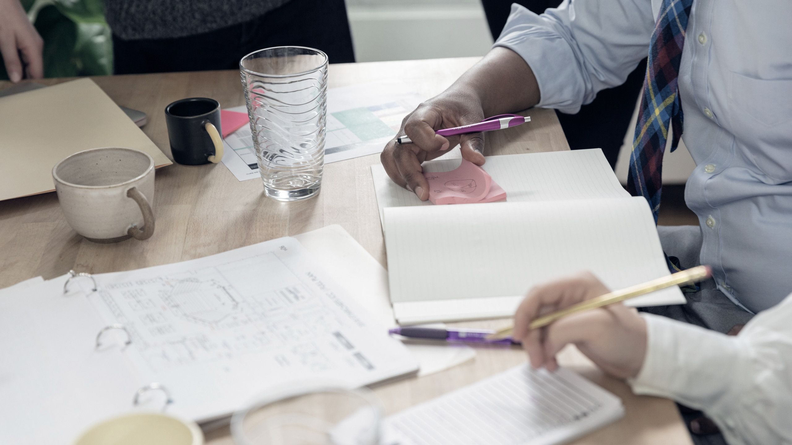 Servicios profesionales: reunión de trabajo con planos impresos, libretas y café sobre la mesa.